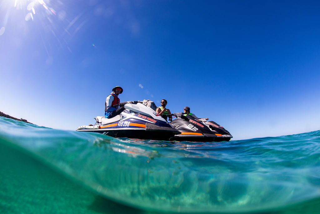 Two people on jet skis in clear blue ocean under a sunny sky.